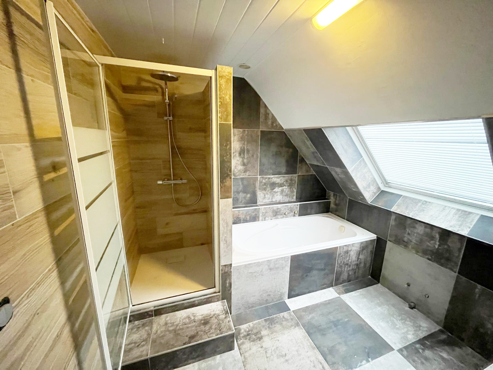 Salle de bains en combles avec douche en carrelage imitation bois et baignoire encastrée