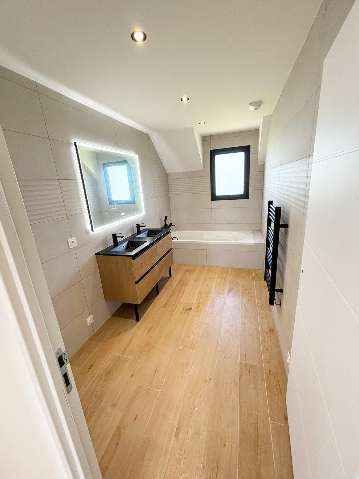 Salle de bains avec double vasque noire, baignoire et miroir LED réalisée à Lorient