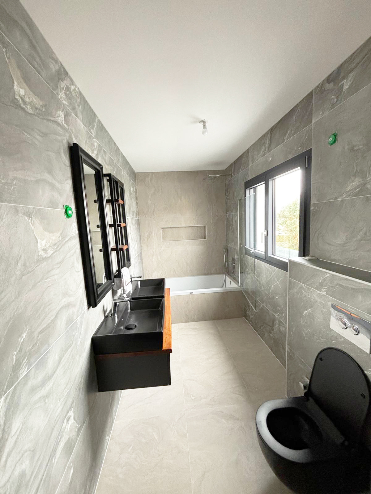 Salle de bains avec double vasque noire, baignoire et WC suspendu
