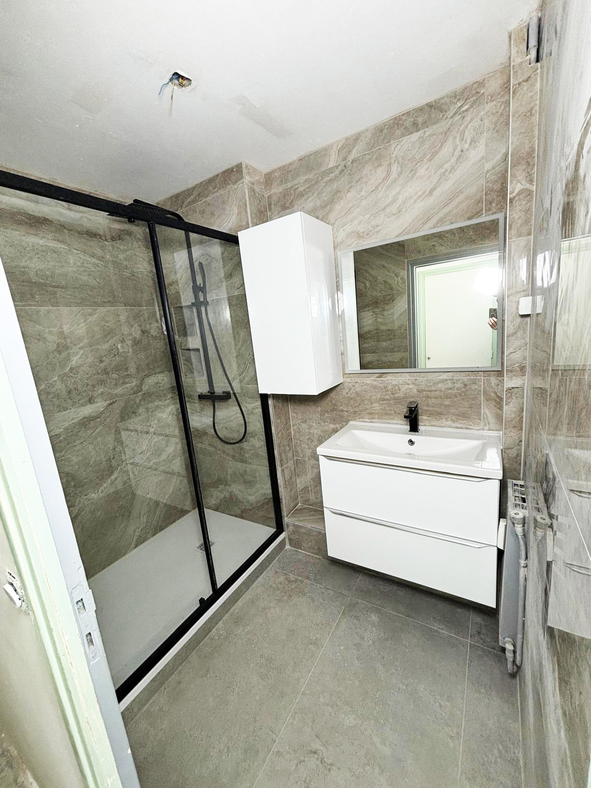 Salle de bains avec douche à porte coulissante noire et meuble blanc suspendu à Lorient