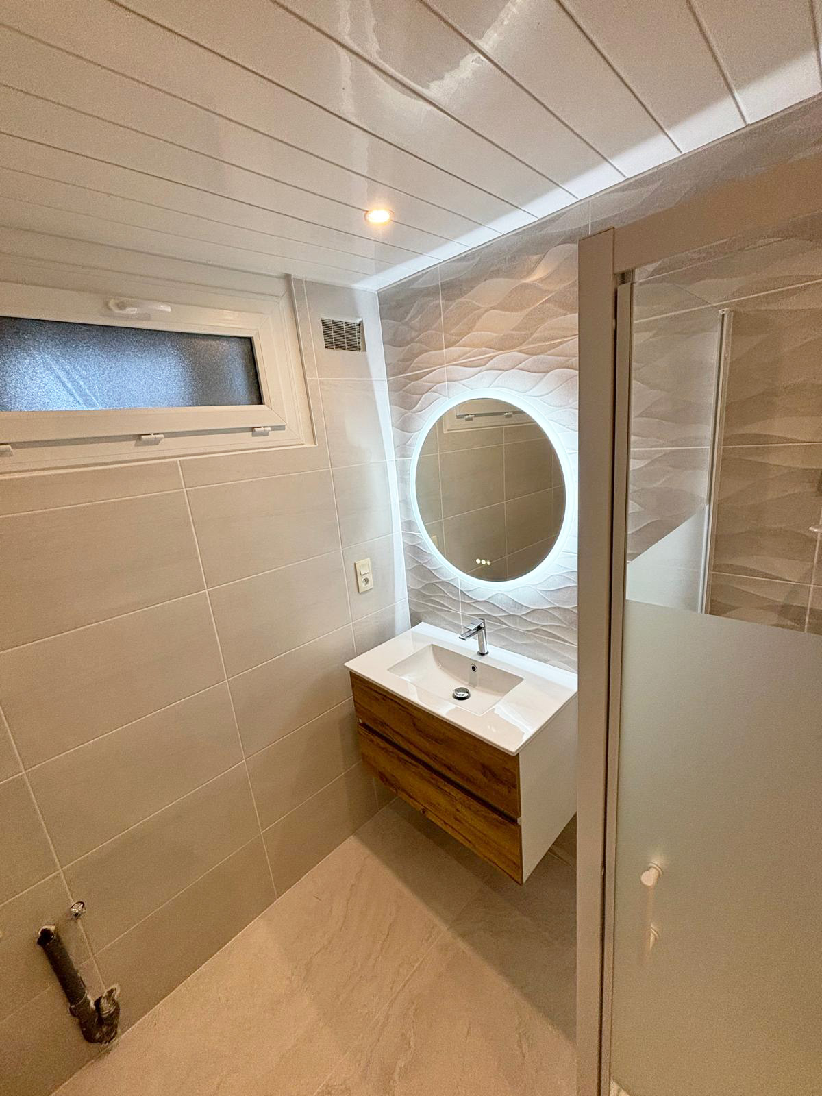 Salle de bains rénovée par SaniBreizh à Lorient : meuble vasque bois et miroir rond rétroéclairé